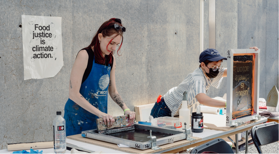Two people at a screen printing station printing t-shirts.