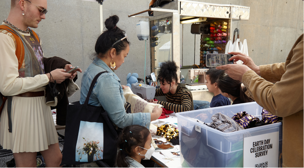 People in line at the repair station and Makayla Wray sitting at the table sewing while surrounded by supplies.
