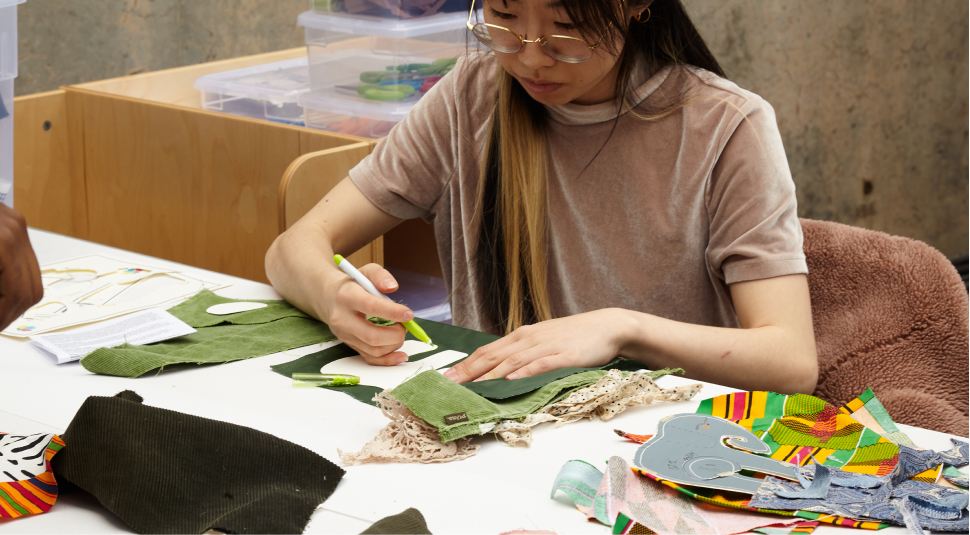 A person sitting at a table tracing patterns on fabric swatches.