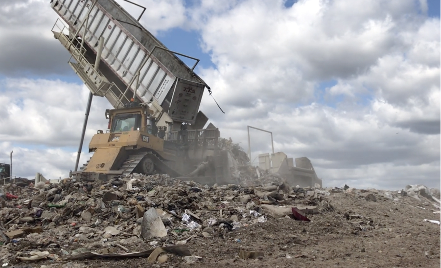 An image of a truck dumping garbage into a landfill pile. The sky is blue and filled with billowy clouds.